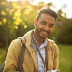 An Indian man is holding a camera and smiling